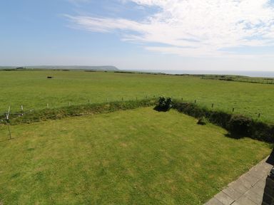 A grassy lawn area with a clothesline and fields extending to the horizon under a partly cloudy sky at Trefollwyn Mawr in Abersoch