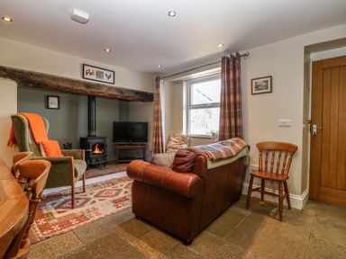A living room with a leather sofa an armchair a wood-burning stove and a television at Trefollwyn Mawr in Abersoch