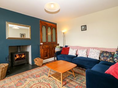 A living room with a blue sofa pillows a wooden coffee table a fireplace and a wooden cabinet at Trefollwyn Mawr in Abersoch