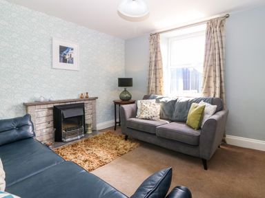 A living room with two sofas a fireplace a side table with a lamp and a window with curtains at Trefollwyn Mawr in Abersoch