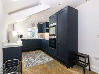 A kitchen with dark cabinets a patterned rug and a small window at Trefollwyn Mawr in Abersoch