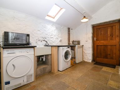 A utility room with a washing machine dryer microwave sink and wooden door at Trefollwyn Mawr in Abersoch