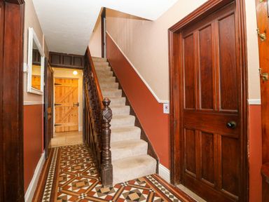A hallway with patterned tile floor a carpeted staircase and wooden doors at Trefollwyn Mawr in Abersoch