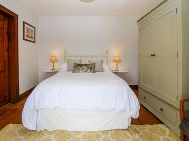 A bedroom with a double bed white bedding bedside tables lamps a green wardrobe and a wooden door at Trefollwyn Mawr in Abersoch