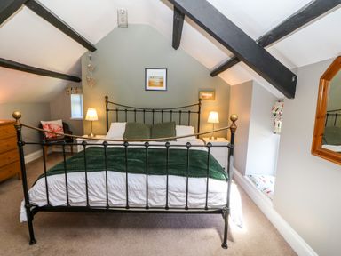 A bedroom with a metal bed frame two bedside tables with lamps a wooden chest of drawers and a chair at Trefollwyn Mawr in Abersoch