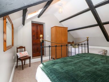 A bedroom with two beds a wooden wardrobe a wooden chair with a pillow a mirror on the wall and exposed ceiling beams at Trefollwyn Mawr in Abersoch