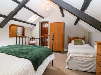 A bedroom with two beds wooden wardrobe mirror and exposed ceiling beams at Trefollwyn Mawr in Abersoch