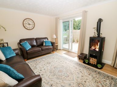 A living room with brown leather sofas blue cushions a patterned rug a clock on the wall and a wood burning stove at 14 The Maltings in Rothbury