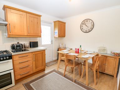 A kitchen with wooden cabinets a dining table with chairs and a wall clock at 14 The Maltings in Rothbury