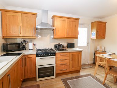 A kitchen with wooden cabinets a stove a microwave and a dining table at 14 The Maltings in Rothbury