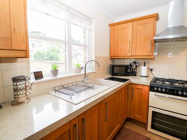 A kitchen with wooden cabinets a double sink stove oven microwave and windowsill plants at 14 The Maltings in Rothbury