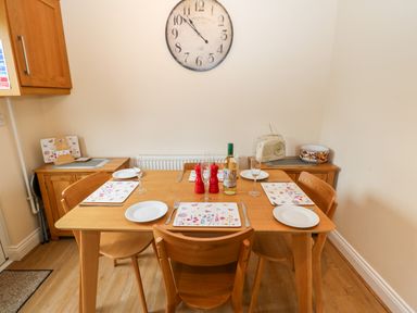 A dining room with a wooden table set for four with plates glasses placemats and a bottle in front of a wall clock at 14 The Maltings in Rothbury