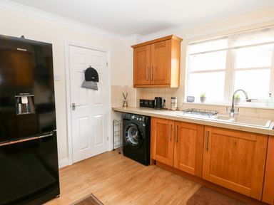 A kitchen with wooden cabinets a black washing machine a black refrigerator and a sink under a window at 14 The Maltings in Rothbury