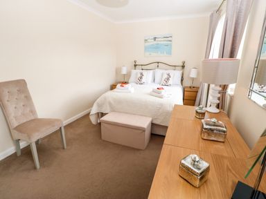 A bedroom with a bed with pillows and folded towels a chair a bedside table with lamps and a wooden dresser with decorative jars at 14 The Maltings in Rothbury