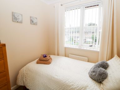 A bedroom with a bed with folded towels and pillows next to a window with vertical blinds at 14 The Maltings in Rothbury