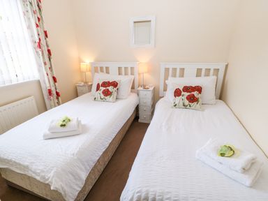 A bedroom with two single beds each with white bedding and poppy flower cushions at 14 The Maltings in Rothbury