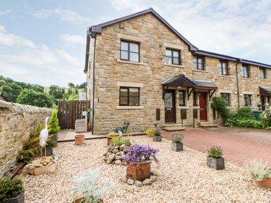 A stone exterior of a townhouse with a gravel garden and potted plants at 14 The Maltings in Rothbury