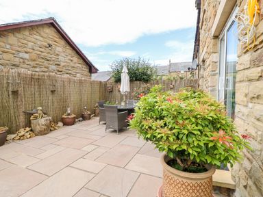A patio area with outdoor table and chairs potted plants and a stone wall at 14 The Maltings in Rothbury