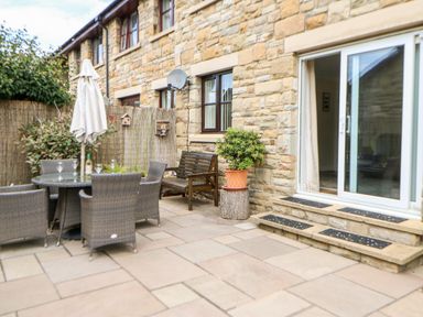 An outdoor patio area with a table and chairs a bench a potted plant and sliding glass doors at 14 The Maltings Rothbury