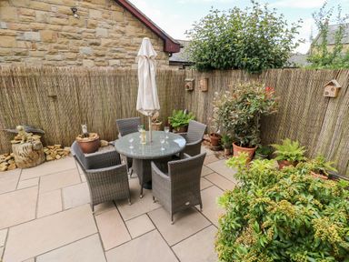 An outdoor patio with a round glass table and four wicker chairs surrounded by potted plants at 14 The Maltings in Rothbury