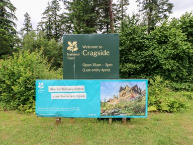 An outdoor sign welcoming visitors to Cragside with opening hours and information about Britain's original smart home at Cragside