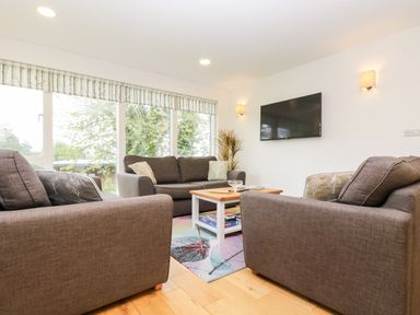 A living room with three gray sofas a wooden coffee table a wall mounted television and large windows at Beech in Truro