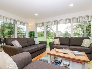 A living room with brown sofas a wooden coffee table and large windows showing greenery at Beech in Truro