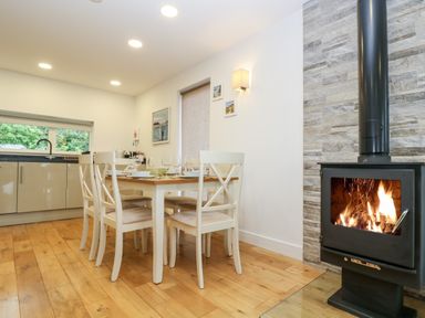 A dining area with a wooden table set for six and a wood-burning stove in a kitchen with wooden floors at Beech in Truro