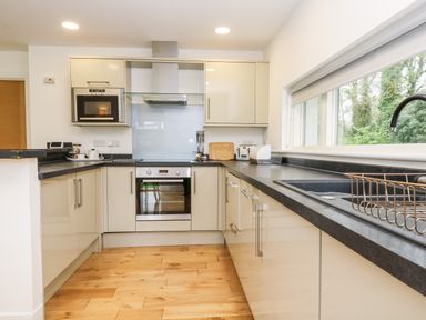 A kitchen with wooden floor black countertops built in oven microwave and a window with a sink and a drying rack at Beech in Truro