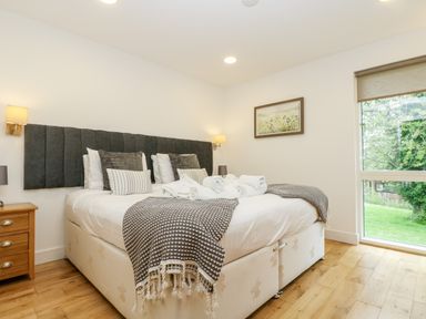A bedroom with a double bed pillows bedside table and window showing green outside at Beech in Truro