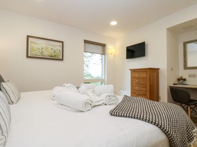 A bedroom with a bed with towels and a blanket a wooden chest of drawers and a wall-mounted television at Beech in Truro