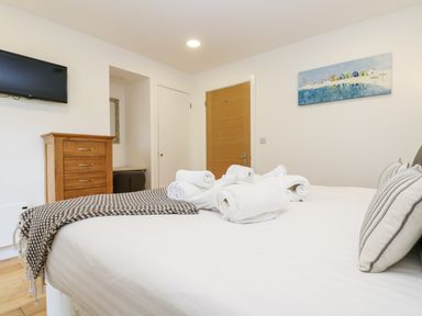 A bedroom with a bed with pillows and towels a wooden dresser and a wall mounted television at Beech in Truro