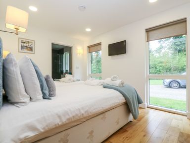 A bedroom with a bed and towels on it a wall mounted tv and a window showing trees and a car at Beech in Truro