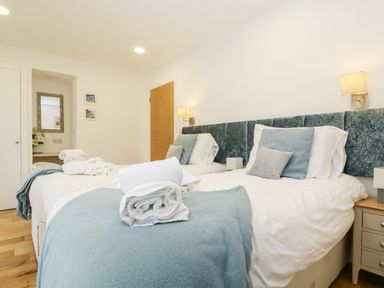 A bedroom with two single beds with blue throws and pillows bedside tables and a door at Beech in Truro