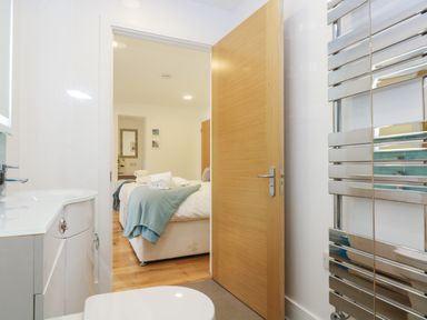 A bathroom with a white sink and toilet a wooden door open to a bedroom with a bed covered in white and blue linens at Beech in Truro