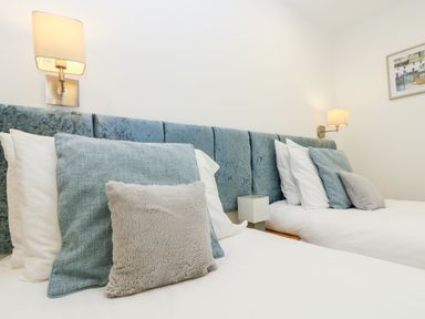 Two beds with blue and gray pillows against a blue upholstered headboard with wall lamps and a framed picture on the wall at Beech in Truro