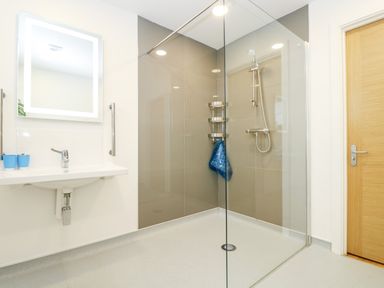 A bathroom with a walk in shower a glass partition a wall mounted sink with two blue cups and a mirror at Beech in Truro