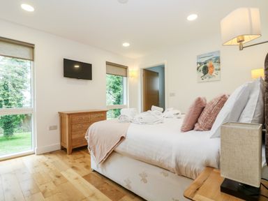 A bedroom with a double bed pillows bedside table wooden chest of drawers and wall-mounted television at Beech in Truro