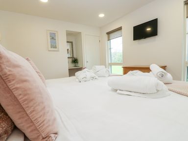 A bedroom with a bed and pink pillows white towels on the bed a wall mounted tv and a wooden chest at Beech in Truro