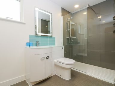 A bathroom with a white toilet cabinet sink and glass shower enclosure with tiled walls at Beech in Truro