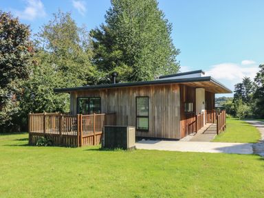 A wooden house with a deck and surrounding grass and trees at Beech in Truro
