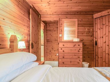 A bedroom with wooden walls a bed with white linens a chest of drawers a mirror and a lamp at Rose Lodge in Milton on Stour