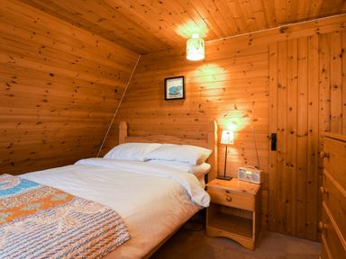 A bedroom with a bed white bedding wooden walls and a nightstand with a lamp and radio at Rose Lodge in Milton on Stour