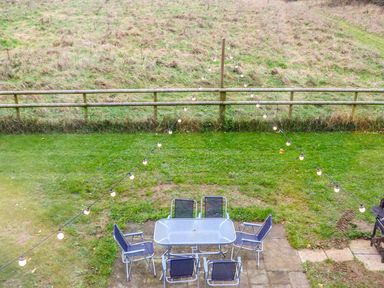 An outdoor patio with a glass table and six chairs on grass with string lights overhead at Rose Lodge in Milton on Stour