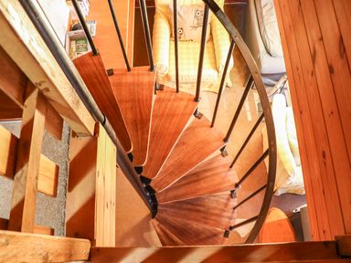 A spiral wooden staircase with metal railings leading down to a seating area with armchairs and a table at Rose Lodge in Milton on Stour