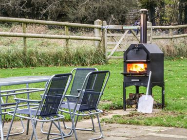 A patio with four metal chairs and a firewood oven burning at Rose Lodge in Milton on Stour