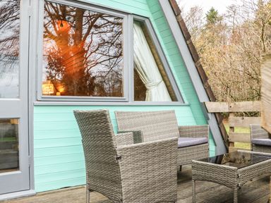 Outdoor seating with wicker chairs and table on wooden deck outside a mint green cabin at Rose Lodge in Milton on Stour
