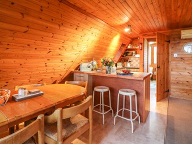 A wooden dining table with chairs and a kitchen counter with stools in a wooden room at Rose Lodge in Milton on Stour