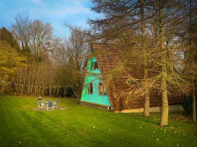 A green a frame house near trees and a grassy yard with outdoor table and chairs at Rose Lodge in Milton on Stour