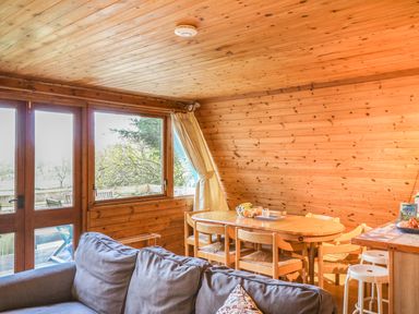 A wooden dining table with chairs and a fruit bowl next to a gray sofa in a wooden room with windows at Rose Lodge in Milton on Stour